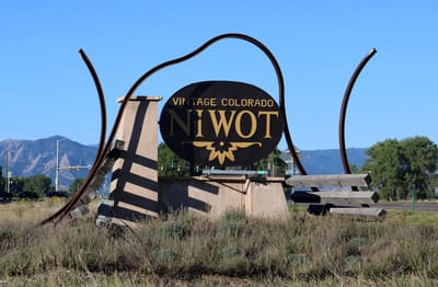 The Vintage Colorado Niwot gateway sculpture, a steel arch over an oval sign, with the Flatirons behind it