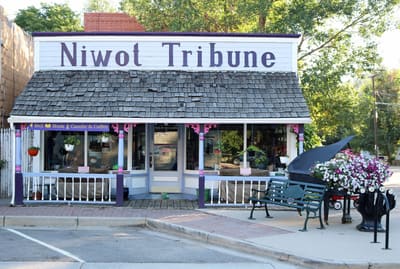 The Niwot Tribune false-front building on Second Avenue with a shingled porch roof, painted columns and a grand piano on the sidewalk